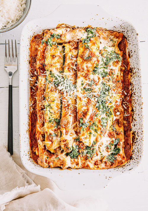 Zucchini-Lasagne mit Bolognese und goldbraunem Mozzarella in einer weißen Auflaufform, von oben fotografiert - mit gehackter Petersilie bestreut