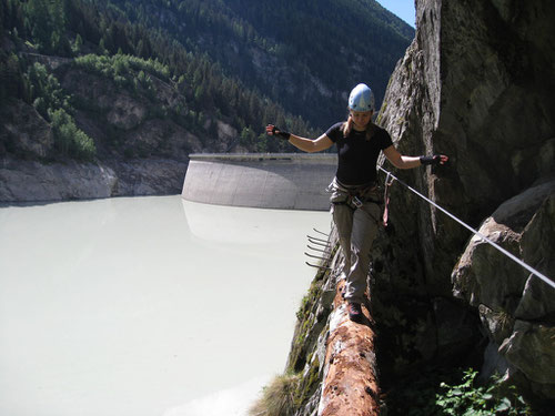 Balancieren auf dem Baumstamm. Im Hintergrund die Staumauer des Gibidum-Stausees