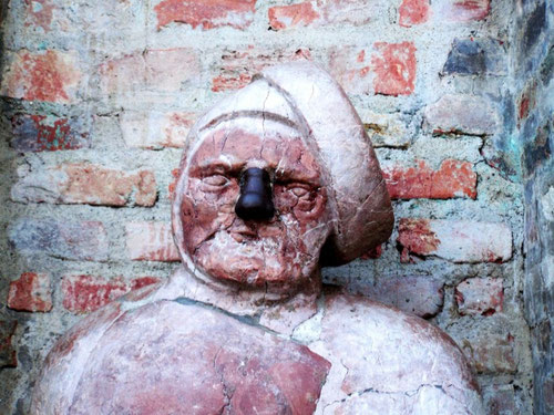 Detaillierte Nahansicht des geschichtsträchtigen Augsburger Standbilds „Stoinarne Ma“ (Steinerner Mann). Die Büste aus rötlichem, verwittertem Stein an einer alten Ziegelmauer zeigt die Legende des versteinerten Bäckers. Ein zentraler Punkt auf der Sagent