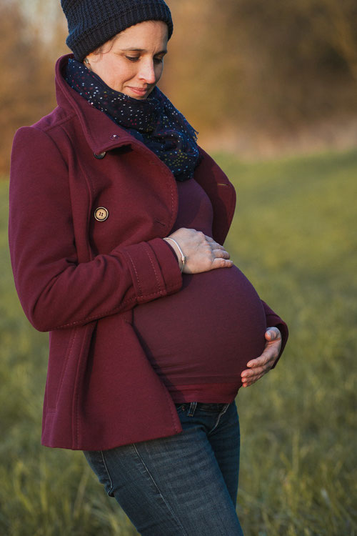 Schwangere hält ihren Babybauch mit beiden Händen fest.