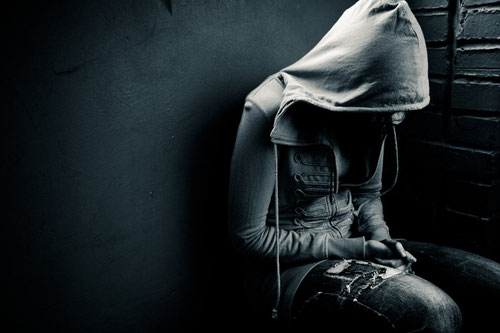 person mit kaputze über dem kopf sitzt in der ecke