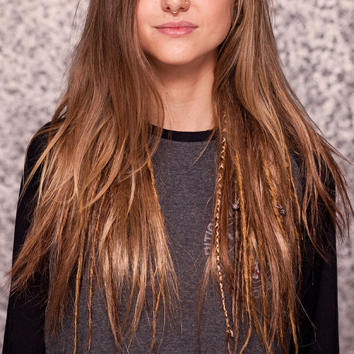 Junge Frau mit langen, natürlichen braunen Haaren und einigen dezenten Single-Ended Dreads mit Boho-Verzierungen. Semipermanente Dreads, natürlich, schonend fürs Eigenhaar.
