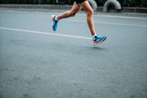 Man sieht die Beine eines Sportlers, der auf der Straße joggt.