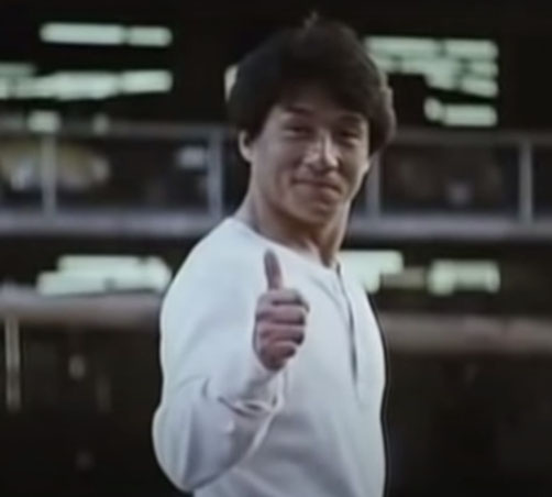 Auf dem Bild ist Jackie Chan, der mit einem Lächeln und gehobenen Daumen in die Kamera guckt.