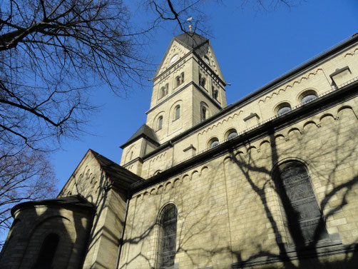 Hinter ein paar Baumästen ragt der neuromanische Kirchturm in den Himmel.