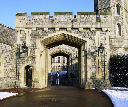 A historic stone gateway with an arched entrance, flanked by two lanterns, leads into a castle courtyard.