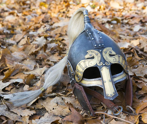 A detailed Viking-style helmet with gold accents and horse designs lies on fallen autumn leaves.