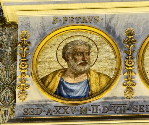 Mosaic portrait of Saint Peter with a halo, framed in gold with Latin inscription beneath on a decorative church wall.