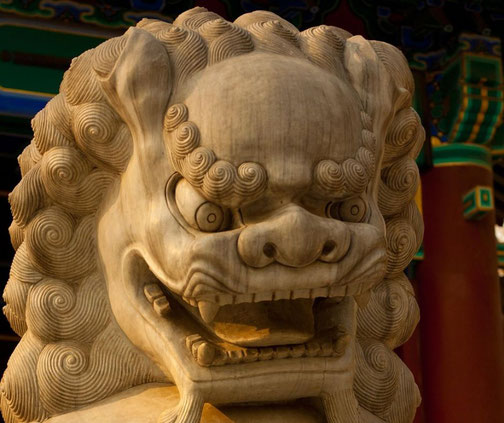 A close-up of a stone Chinese guardian lion statue, known as a foo dog, with intricate curls and a fierce expression.