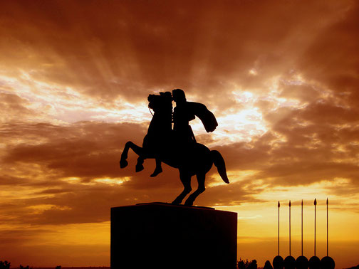 Silhouette of a rider on a rearing horse atop a pedestal, set against a dramatic sunset sky with rays piercing the clouds.