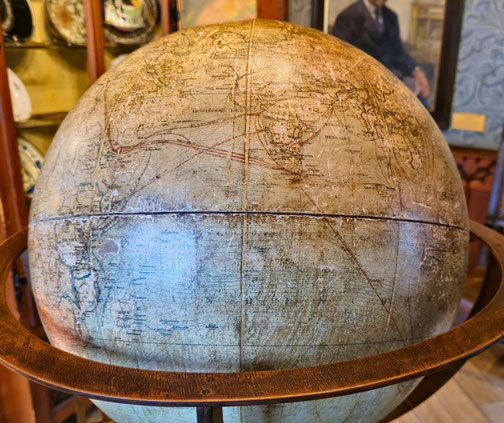 Detailed globe mounted on a metal frame, surrounded by ornate wooden furniture and historical decor in a museum or study setting.