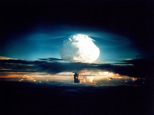 A towering, glowing mushroom cloud rises into a dark sky during a high-yield nuclear explosion over the ocean.