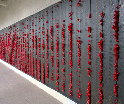 A metal memorial wall lists fallen soldiers' names with red poppies placed in the engraved letters.