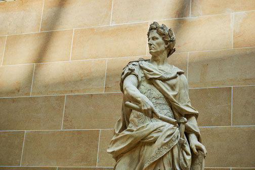 Marble statue of a Roman figure in detailed armor and laurel wreath, gripping a baton and looking to the side.