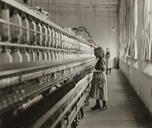 A young girl working at a cotton mill, standing beside a row of spinning machines.