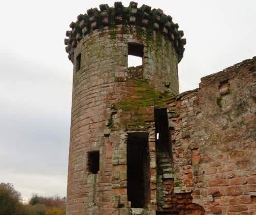Weathered stone tower ruin with visible moss growth and missing sections, set against a cloudy sky and forest backdrop.