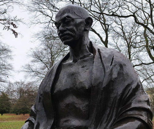 A close-up of a bronze statue of Mahatma Gandhi in Geneva, Switzerland. His contemplative expression, draped shawl, and wire-rimmed glasses highlight his iconic presence and wisdom.