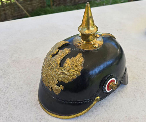 A black German pickelhaube helmet with a gold spike and eagle crest rests on a light surface.
