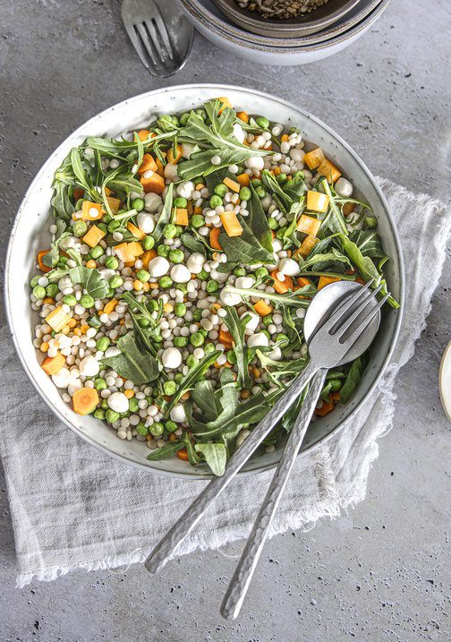 Herbstlicher Pearl-Couscous-Salat mit Mozzarella, Rucola und Gemüse in einer Schüssel serviert.