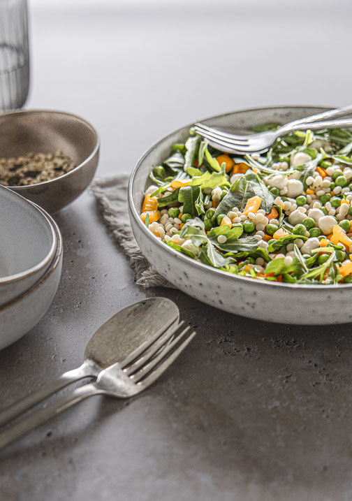 Herbstlicher Pearl-Couscous-Salat mit Mozzarella, Rucola und Gemüse in einer Schüssel serviert.
