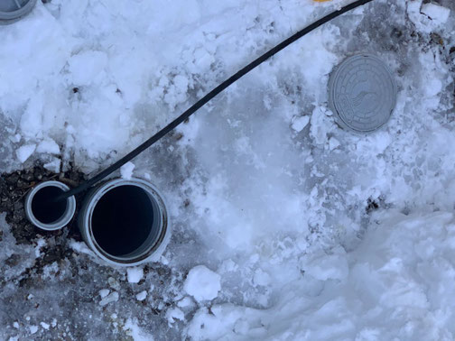 積雪で汚水桝が埋まった現場を除雪し、桝を開けて高圧洗浄ホースを挿入している冬の作業風景。