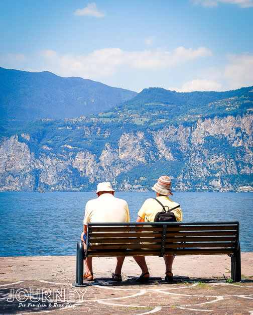 Ein Paar sitzt auf einer Bank am Ufer des Gardasees.