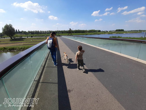 Frau mit Hund und Kind geht über eine Brücke mit Glasbrüstung in Venlo.