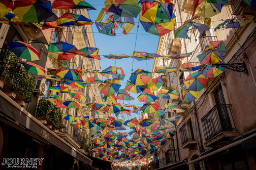 Bunte Regenschirme sind über eine Straße in Catania gespannt.
