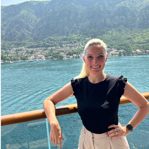 Anne Fischer von Emocean Cruises steht an Deck der Explora I mit Blick auf die Küste und die grünen Berge der Adria.