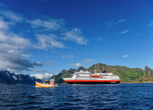 MS OTTO SVERDRUP unter blauem Himmel und vor grün bedeckten Fjorden - ein kleines Fischerboot im Vordergrund