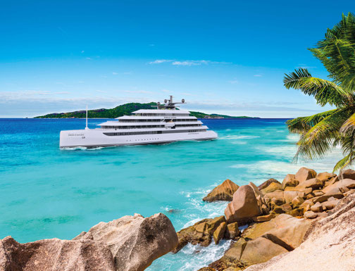 Tropische Szenerie mit Emerald Sakara Yacht im türkisfarbenen Meer. Felsige Ufer im Vordergrund und rechts im Bild eine Palme.