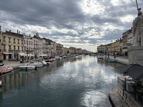 Blick über den Canal Royal in Sète mit Booten, historischen Häuserfassaden und wolkenverhangenem Himmel.