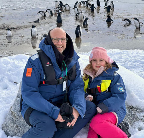 Timo Clarén und Tochter Lina mit Pinguinen im Hintergrund, bei einem Landausflug in der Antarktis