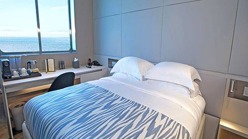 Moderne Oceanview Kabine auf der Superyacht Emerald Kaia mit komfortablem Bett, Arbeitsplatz und Meerblick durch das große Fenster.