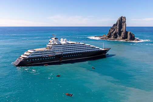 Scenic Eclipse fährt im kristallblauem Meer an einem Felsen vorbei