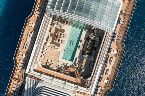 Draufsicht auf das Pooldeck der Explora I von Explora Journeys mit Liegen, Lounges und Infinity-Pool.