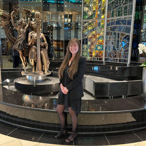 Jessica Staffel von Emocean Cruises steht in der eleganten Lobby der Crystal Serenity vor einer kunstvollen Skulptur und farbenprächtigen Glaswand.