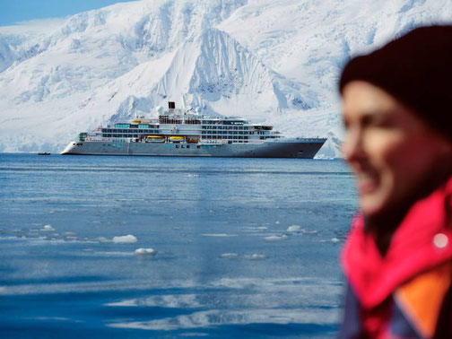 Silversea Expeditionsschiff vor schneebedeckten Bergen in der Antarktis, im Vordergrund eine Person in warmer Kleidung.