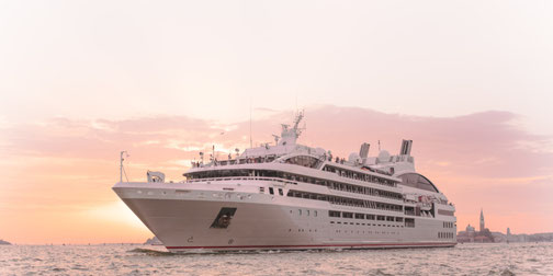 Ponant-Schiff der Boreal-Klasse im Sonnenuntergang und einer Hafenstadt im Hintergrund