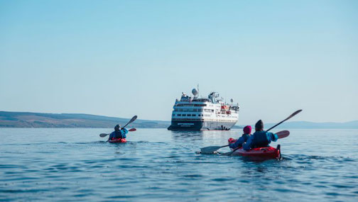 Zwei Kajaks auf dem Meer vor einem Expeditionsschiff von HX Hurtigruten Expeditions