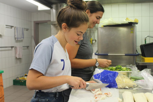 Schülerin und Mitarbeiterin bereiten zusammen Mahlzeiten zu – gemeinsames Kocherlebnis im erlebnispädagogischen Programm