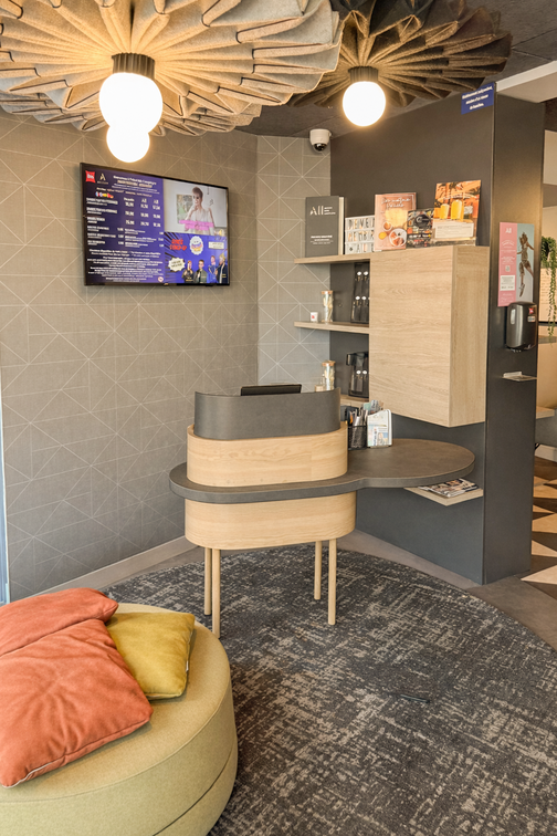 Comptoir d’accueil arrondi en bois clair et plateau anthracite, installé dans le hall d’un hôtel à Compiègne.