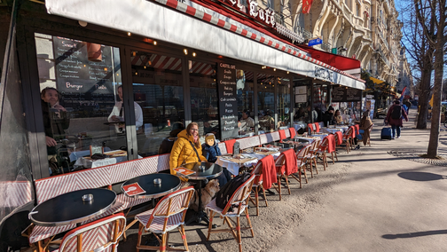 Eine Frau, in gelber Jacke, sitzt mit ihrem Sohn in einem Café in Paris.