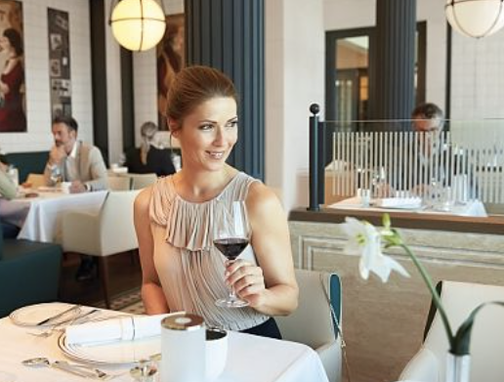 Lächelnde Frau sitzt im Restaurant am Tisch mit Weinglas in der linken Hand