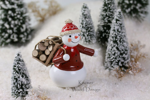 Handgefertigter Erzgebirge-Schneemann aus Holz mit roter Jacke und Schlitten voller Holzscheite in winterlicher Landschaft
