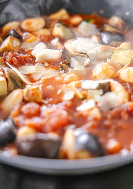 Toskanisches Gemüse-Ragout mit Aubergine, Zucchini, weißen Bohnen und Parmesan, serviert mit frischem Basilikum und knusprigem Baguette