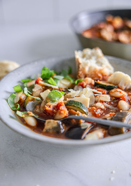 Toskanisches Gemüse-Ragout mit Aubergine, Zucchini, weißen Bohnen und Parmesan, serviert mit frischem Basilikum und knusprigem Baguette