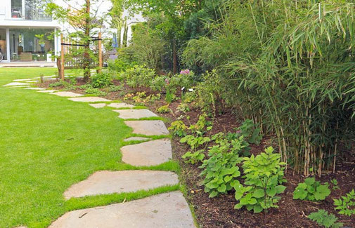 Polygonalplatten aus Grauwacke führen entlang der geschwungenen Rasenkante, vorbei an Sträuchern, durch den Garten