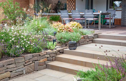 Podesttreppe mit breite Blockstufen aus Naturstein gleichen den Höhenunterschied von Terrasse und Garten aus