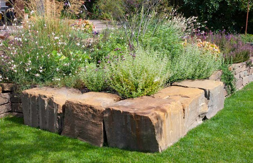 Die Trockenmauer aus großen Grauwacke-Steinen ist Beeteinfassung und Sitzgelegenheit in Einem 